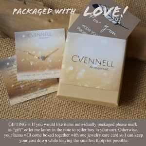 May include: A small, white box with a gold glitter background and the text "CVENNELL be inspired..." printed on it. The box is closed and has a gold chain necklace with a small, clear stone pendant inside. The box is sitting on a brown burlap surface. The text "PACKAGED WITH LOVE!" is printed on a brown card with a feather design. The text "Hope you Please You." is also printed on the card.