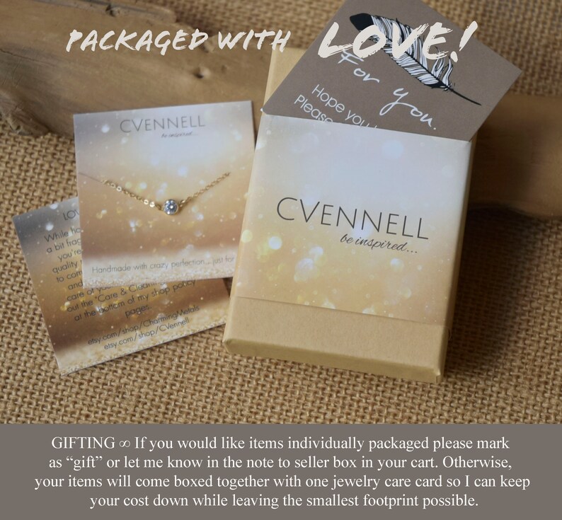 May include: A small, white box with a gold glitter background and the text "CVENNELL be inspired..." printed on it. The box is closed and has a gold chain necklace with a small, clear stone pendant inside. The box is sitting on a brown burlap surface. The text "PACKAGED WITH LOVE!" is printed on a brown card with a feather design. The text "Hope you Please You." is also printed on the card.