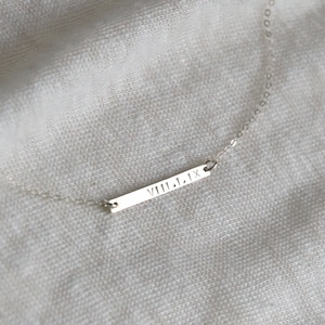 May include: A silver necklace with a bar pendant engraved with the Roman numeral date "VIII.1.1X".