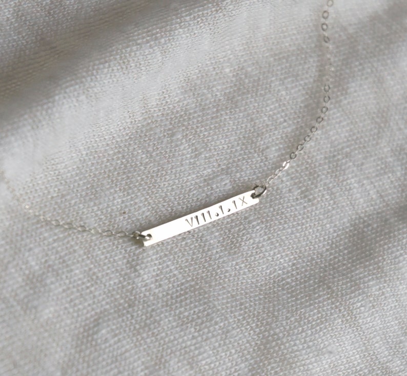 May include: A silver necklace with a bar pendant engraved with the Roman numeral date "VIII.1.1X".