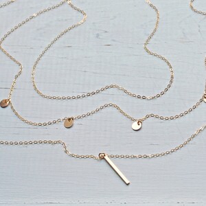 May include: A gold chain necklace with multiple small round charms and a long, thin bar pendant.