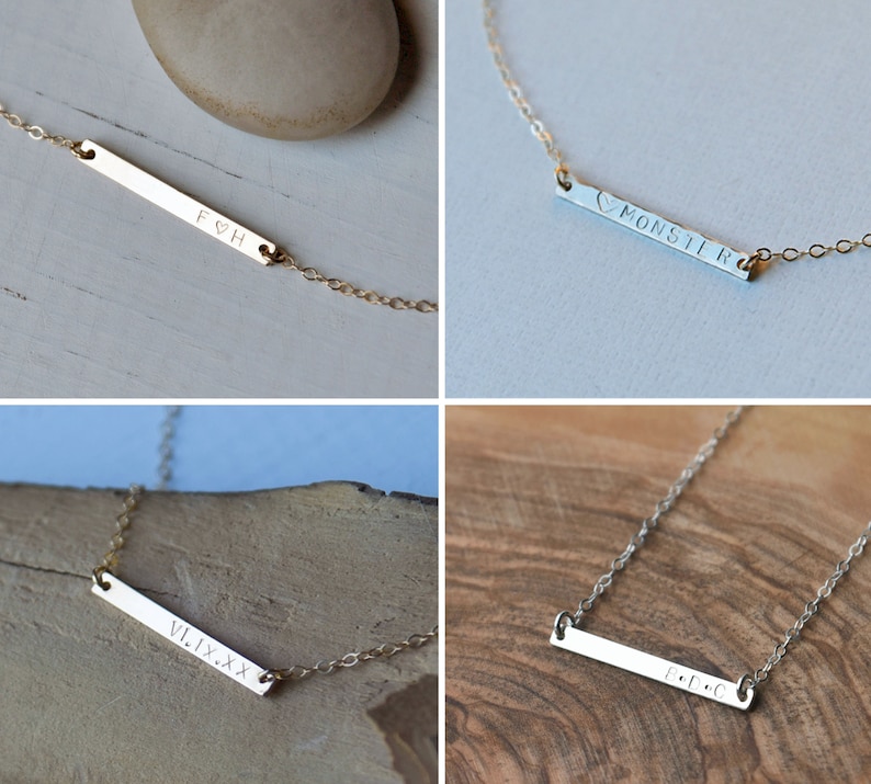 May include: Four gold bar necklaces with different engraved text. The necklaces are on a white and wood background. The text on the necklaces reads "F&H", "&hearts;MONSTIR", "VI.IX.XX", and "E.D.C".