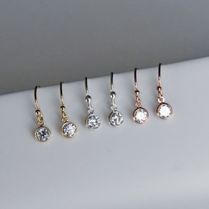 May include: Five pairs of dangle earrings with small round clear stones. The earrings are in gold, silver, and rose gold.