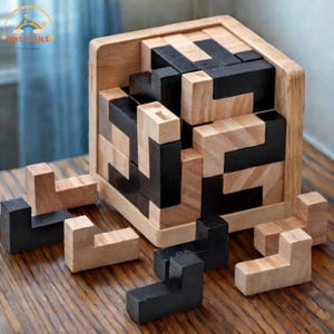 Może przedstawiać: Drewniana gra logiczna z ramą w kształcie kostki. Puzzle składają się z kilku bloków w kształcie litery L w naturalnym drewnie i czerni. Niektóre bloki znajdują się poza ramą, co sugeruje, że układanka jest w trakcie. Gra znajduje się na drewnianej powierzchni.