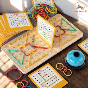 May include: Wooden pegboard with colorful rubber bands forming geometric shapes. Includes cards with design examples, a blue bell, and a pile of assorted rubber bands. Educational toy for children.