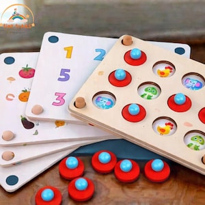 Może przedstawiać: Drewniana zabawka edukacyjna z kolorowymi ilustracjami i cyframi. Zestaw zawiera trójkątną tablicę z obrazkami zwierząt i kołkami, a także pasujące czerwone i niebieskie elementy. Dodatkowe tablice przedstawiają owoce i liczby.