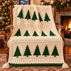 May include: A cream-coloured crocheted throw blanket featuring a repeating pattern of dark green pine trees. The blanket has a textured stitch design, a solid green border along the bottom edge, and decorative tassels at each of the two bottom corners.