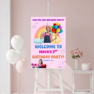 Puede incluir: Un letrero rosa de bienvenida a una fiesta de cumpleaños sobre un caballete. El letrero dice "¡Bienvenida a la 3ª fiesta de cumpleaños de Maya!" con la fecha del 15 de diciembre de 2025. El letrero tiene un arcoíris, globos e imágenes de una niña y personajes de Barrio Sésamo.
