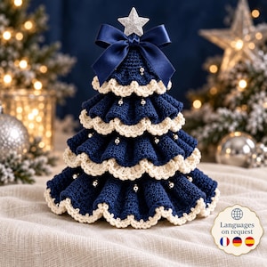 May include: A tiered crochet Christmas tree in navy blue with cream-colored scalloped edges. The tree is decorated with small silver beads and topped with a dark blue satin ribbon bow and a glittery silver star ornament at the very peak.