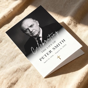 以下が含まれることがあります： 男性の肖像画が描かれた、白黒の追悼カード。「Celebrating The Life of Peter Smith」と日付、金の十字架が書かれています。カードは折りたたまれ、ベージュ色の表面に置かれています。