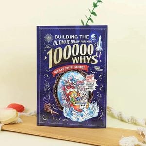 May include: A hardcover book titled "BUILDING THE ULTIMATE BRAIN FOR KIDS 100000 WHYS! FUN AND JOYFUL SCIENCE" is displayed. The cover is dark blue with colorful illustrations of cartoon animals and a rocket ship. The book is on a wooden surface.