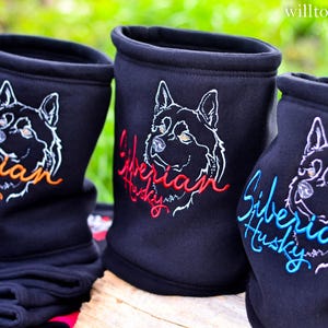 Puede incluir: Cuellos negros con un contorno blanco de la cara de un perro Husky Siberiano y las palabras "Siberian Husky" en escritura naranja, roja y azul. Los cuellos están hechos de una tela oscura y suave.