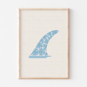 May include: A framed print featuring a light blue surfboard fin with a floral pattern. The fin is set against a cream-colored background, and the frame is a light wood color. The artwork is a minimalist design.