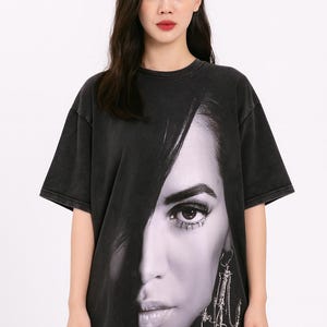 May include: Black oversized t-shirt featuring a black and white close-up of a woman's face. The graphic print covers most of the front of the shirt. The shirt has short sleeves and a crew neck.