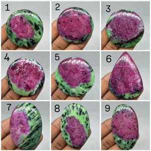 May include: A collection of nine polished ruby in zoisite gemstones, each numbered one through nine. These stones feature vibrant magenta-pink centers surrounded by mottled green and black mineral patterns in various oval and teardrop shapes.
