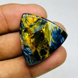 May include: A triangular-shaped gemstone with a striking pattern of yellow, blue, and black swirls. The polished surface reflects light, highlighting the stone's natural colors and textures. This unique gemstone is ideal for jewelry making.