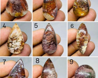 May include: A collection of nine polished garden quartz cabochons labeled one through nine. Each gemstone features unique internal inclusions in shades of deep red, brown, purple, and white, displayed in various teardrop, oval, and round shapes.
