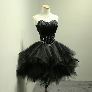 May include: A strapless black dress with a feathered bodice and a layered tulle skirt. The waistline is embellished with a band of sparkling rhinestones. The dress is displayed on a mannequin.