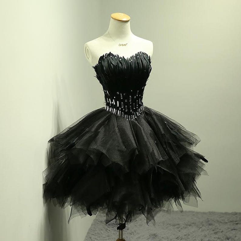 May include: A strapless black dress with a feathered bodice and a layered tulle skirt. The waistline is embellished with a band of sparkling rhinestones. The dress is displayed on a mannequin.