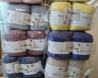 May include: A stack of yarn skeins in various colors, including pink, white, gray, yellow, purple, blue, and green. Each skein is wrapped in clear plastic and labeled with product information. The yarn is labeled as "super cotton".
