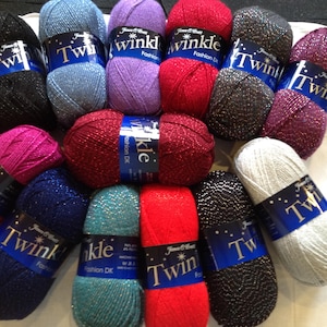 May include: A collection of yarn skeins in various colors, including black, blue, purple, red, and silver. Each skein is labeled with a blue band that reads "Twinkle Fashion DK". The yarn appears to have a metallic sheen.