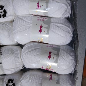 May include: Several skeins of white yarn are packaged in clear plastic. Each skein has a label with a silhouette of a person and the words "Pete Pan". The yarn is tightly wound and appears soft, suitable for knitting or crochet projects.
