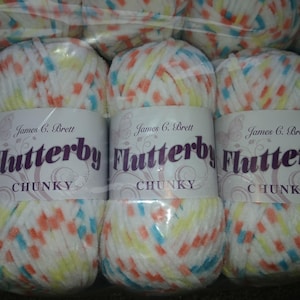 Pode incluir: Vários novelos de fio grosso com um padrão salpicado em branco, laranja, azul e amarelo. Cada novelo tem uma etiqueta que diz "Flutterby CHUNKY" e "James C. Brett".