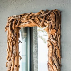 May include: A rectangular mirror with a frame crafted from natural driftwood. The frame is made up of many small, light brown wooden pieces, creating a rustic, textured border. The mirror is mounted on a light grey wall.