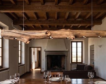 May include: A horizontal pendant light fixture crafted from a single piece of natural, weathered brown driftwood. The log features multiple recessed circular light sources embedded along its underside, suspended by thin wires from the ceiling.