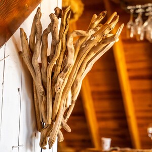 Puede incluir: Un aplique de pared construido con un grupo de ramas de madera flotante de color marr&oacute;n claro y desgastadas, dispuestas en una formaci&oacute;n vertical en forma de abanico. Las piezas de madera natural y nudosa est&aacute;n unidas en una estructura org&aacute;nica.