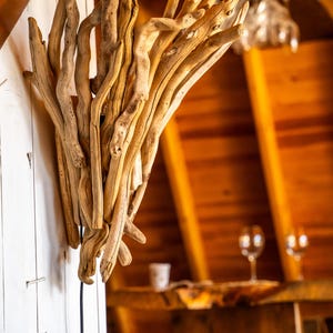 Puede incluir: Un aplique de pared construido a partir de un grupo de ramas de madera flotante de color claro y desgastadas, dispuestas en una formaci&oacute;n vertical en forma de abanico. Las piezas de madera natural var&iacute;an en grosor y textura, con un acabado liso.