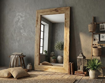 May include: A large rectangular floor mirror with a thick, light-colored natural wood frame. The mirror reflects an interior space with a window, potted plants, and a stone floor. The frame features visible wood grain and texture.