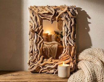 May include: A rectangular wall mirror featuring a frame constructed from numerous pieces of light brown driftwood arranged in an overlapping, textured pattern. The mirror reflects a bedroom interior, and a small candle in a ceramic holder sits nearby.
