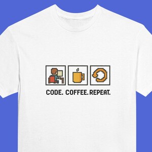 May include: White t-shirt featuring a pixelated design of a person coding, a coffee cup, and a circular arrow. The text "CODE. COFFEE. REPEAT." is printed below the graphics in black.
