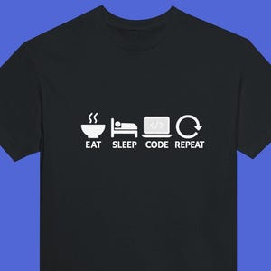 May include: Black t-shirt featuring a white graphic. The graphic shows a bowl, a bed, a laptop with code, and a circular arrow, with the words "EAT SLEEP CODE REPEAT" underneath.