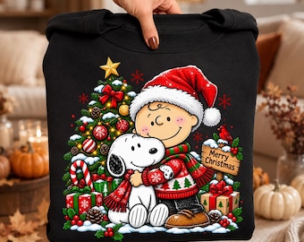 May include: A black sweatshirt featuring a graphic of a cartoon character wearing a Santa hat and a red and green patterned sweater, hugging a white dog. The design includes a decorated Christmas tree, wrapped gifts, and a sign reading Merry Christmas.