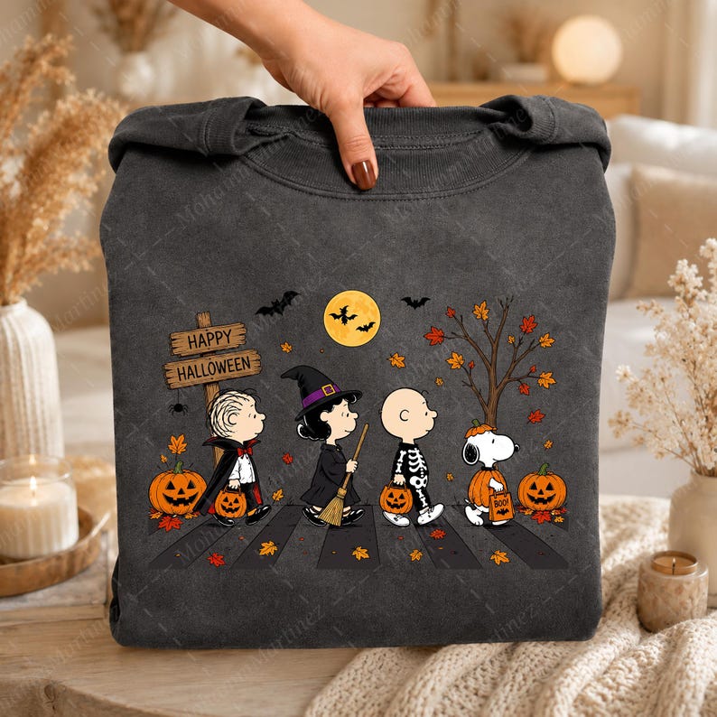 May include: A charcoal gray crewneck sweatshirt featuring a graphic of four cartoon characters dressed in Halloween costumes. The design includes a wooden sign reading Happy Halloween, a yellow moon, bats, orange pumpkins, and autumn leaves.