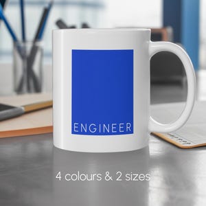 May include: White ceramic mug featuring a blue rectangle with the word "ENGINEER" in white. The mug has a curved handle and the text "4 colours & 2 sizes" is at the bottom. The mug is on a grey surface.