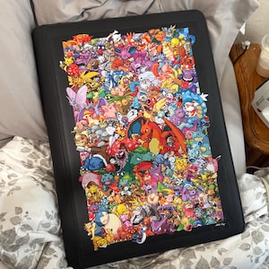 May include: Black binder featuring a colorful collage of various cartoon characters. The binder is rectangular and appears to be made of a sturdy material. The artwork is vibrant and detailed, showcasing a variety of creatures in a playful arrangement.