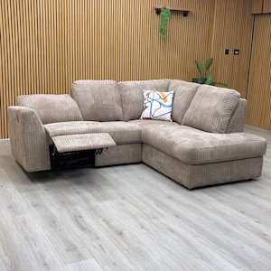 May include: A beige corduroy corner sofa with a recliner. The sofa features a chaise longue and a decorative cushion with an abstract design. The room has wood paneling and a light-coloured floor.