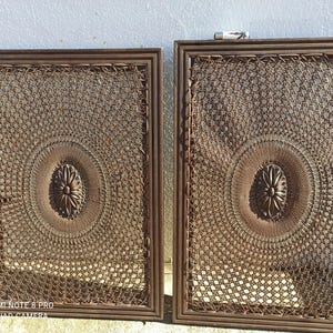 Puede incluir: Dos paneles murales rectangulares con intrincados patrones tejidos en un tono marrón cálido. Cada marco presenta un diseño floral central y un borde detallado, creando una estética vintage. La textura tejida añade profundidad e interés visual.