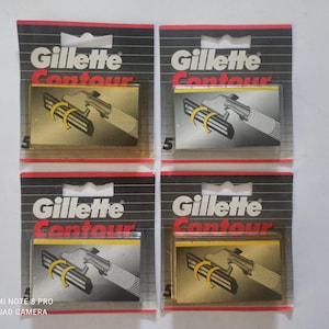 May include: Four packages of Gillette Contour razor blades. Each package has a black and red design with the Gillette Contour logo. The blades are in a gold-colored casing with a silver handle.