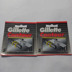 May include: Two packages of Gillette Contour razor blade refills. Each package is black with red accents and features the Gillette logo and the word "Contour" in red. The packages display a diagram of the razor blades and the number "5".