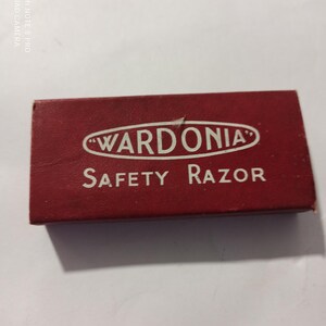 Könnte beinhalten: Eine rechteckige, kastanienbraune Schachtel mit dem Markennamen "WARDONIA" in einem weißen Oval und den Worten "SAFETY RAZOR" in weißer Schrift. Die Schachtel ist leicht abgenutzt.
