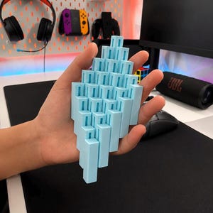 May include: A light blue 3D printed geometric object composed of multiple vertical rectangular pillars of varying heights arranged in a stepped, cascading formation that fits within the palm of a hand.