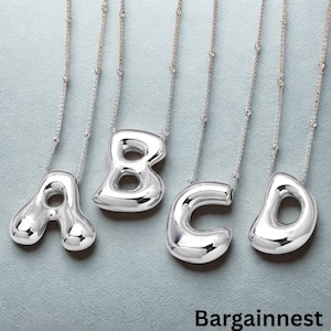 Può includere: Quattro collane argentate con le lettere ABCD. Ogni lettera ha un design arrotondato a forma di bolla, sospesa a una delicata catena. Le collane sono esposte su uno sfondo azzurro. La parola "Bargainnest" è in basso.