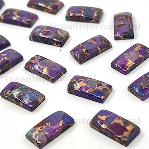 May include: Rectangular purple and gold gemstone cabochons. The stones have a mosaic pattern with shades of purple, blue, and gold. The cabochons are polished and have a smooth surface. The gemstones are arranged on a white surface.