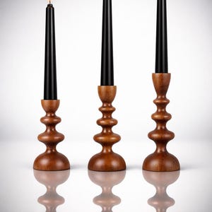 May include: Three wooden candle holders with black candles and lit flames. The candle holders have a tiered, rounded design and a warm brown finish. The candles are tall and slender, with a bright flame.