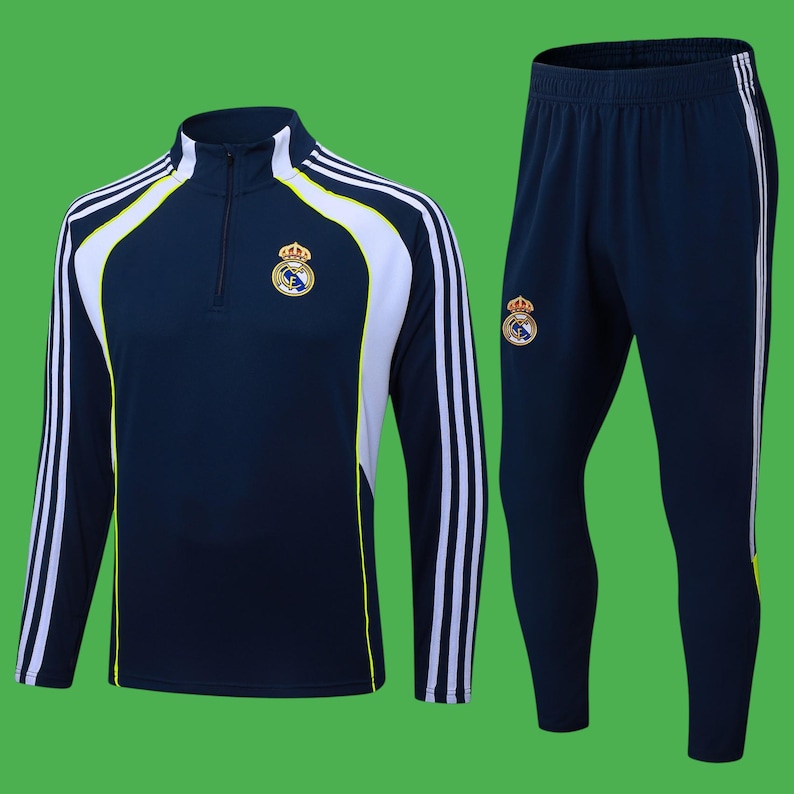 May include: Navy blue athletic tracksuit featuring a long-sleeved top and matching pants. The top has a quarter-zip collar, white and yellow accents, and the team logo on the chest. The pants have white stripes down the side and the team logo.