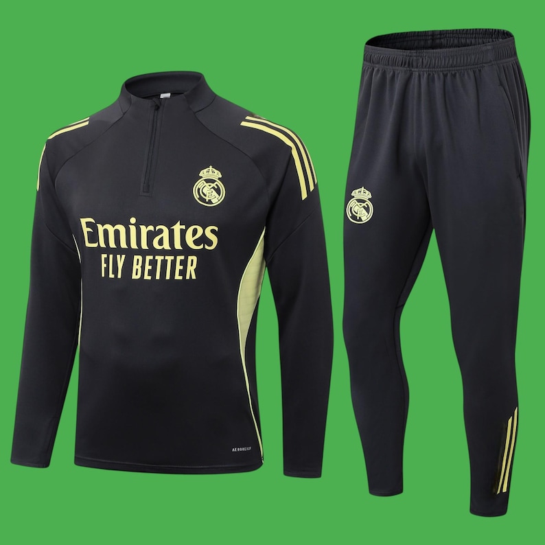 May include: Black athletic tracksuit with gold accents. The top features a half-zip, the text "Emirates FLY BETTER", and a team crest. The matching pants have a team crest and gold stripes. The tracksuit is on a green background.